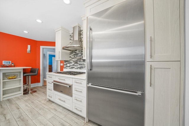 kitchen with white cabinets, appliances with stainless steel finishes, wall chimney range hood, a warming drawer, and tasteful backsplash