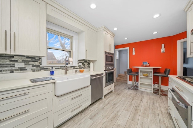 kitchen with stainless steel appliances, a sink, light wood-style floors, light countertops, and decorative backsplash