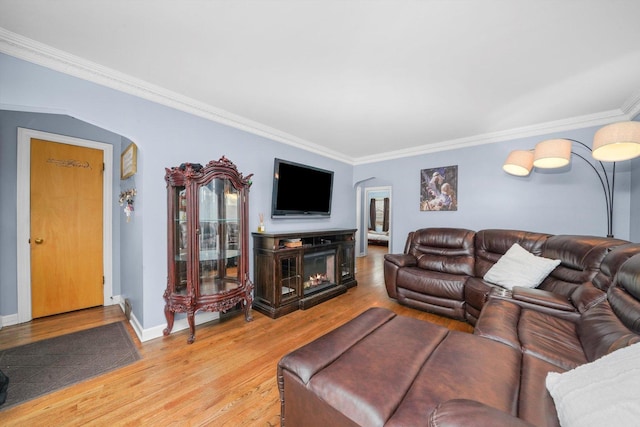 living room featuring baseboards, arched walkways, a glass covered fireplace, ornamental molding, and wood finished floors