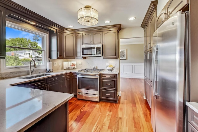 kitchen with a wainscoted wall, light wood finished floors, a sink, stainless steel appliances, and a decorative wall