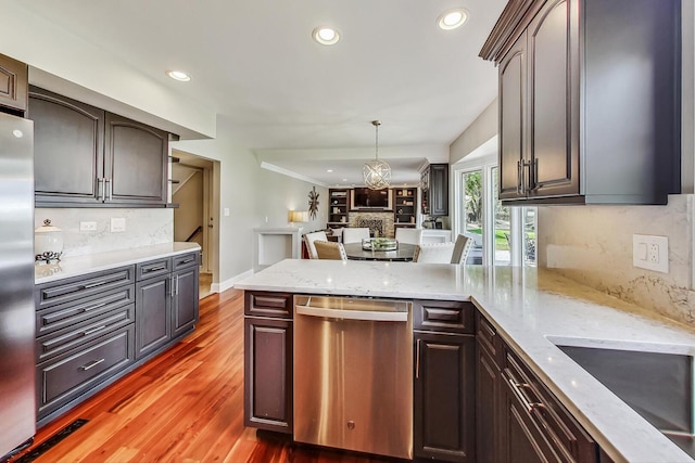 kitchen with tasteful backsplash, light stone counters, light wood-style flooring, appliances with stainless steel finishes, and a peninsula