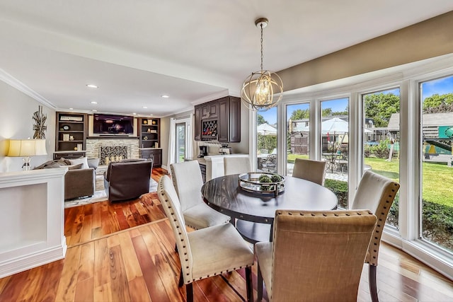 dining room featuring ornamental molding, a stone fireplace, recessed lighting, light wood-style floors, and a notable chandelier