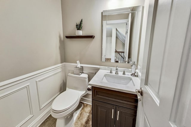 bathroom with a decorative wall, wainscoting, toilet, and vanity