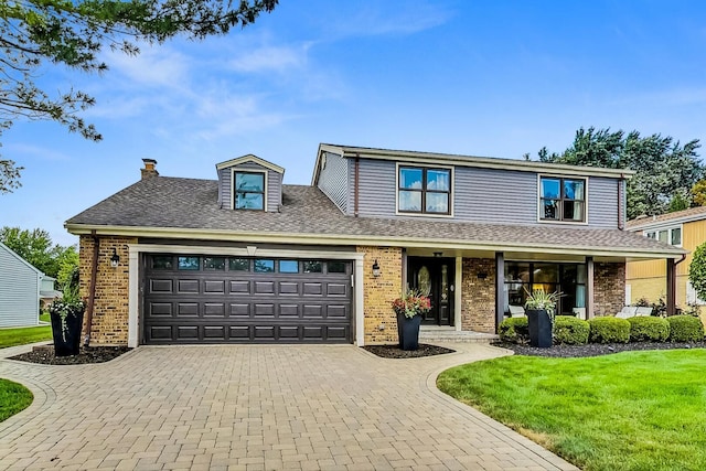 traditional home with decorative driveway, roof with shingles, an attached garage, a front yard, and brick siding