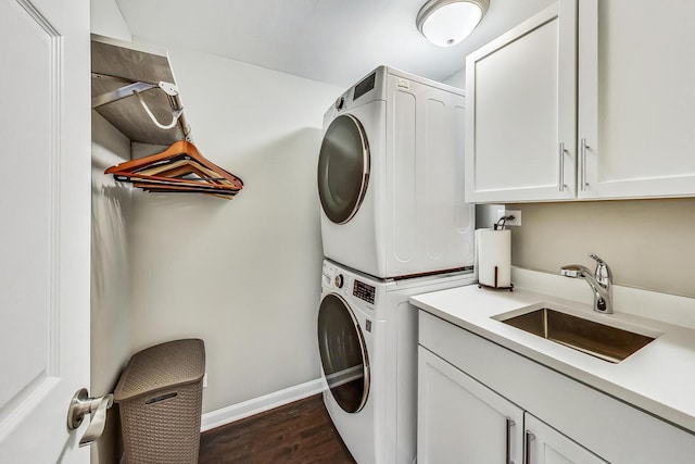 washroom with baseboards, dark wood finished floors, cabinet space, a sink, and stacked washer / drying machine