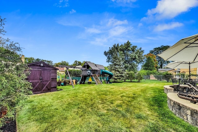 view of yard with a fire pit, a playground, a fenced backyard, an outbuilding, and a storage unit