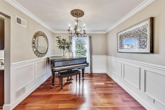 living area with wood finished floors, visible vents, ornamental molding, wainscoting, and a notable chandelier