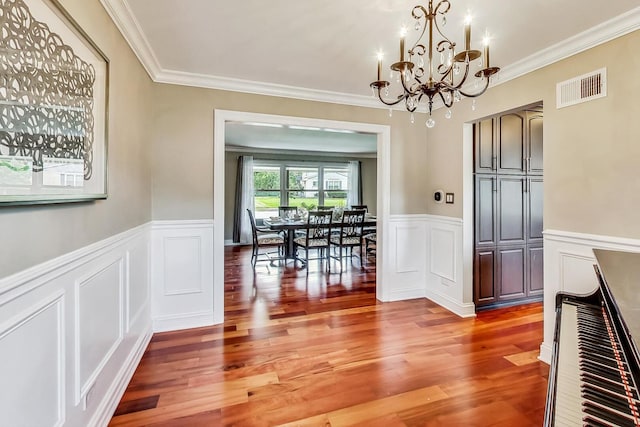 unfurnished dining area with light wood finished floors, visible vents, ornamental molding, wainscoting, and a notable chandelier