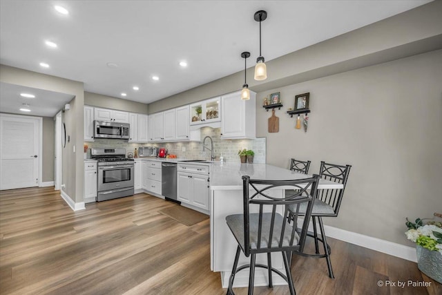 kitchen featuring white cabinets, appliances with stainless steel finishes, a peninsula, a sink, and backsplash