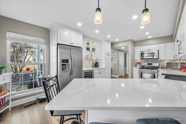 kitchen with wine cooler, white cabinets, light countertops, appliances with stainless steel finishes, and pendant lighting