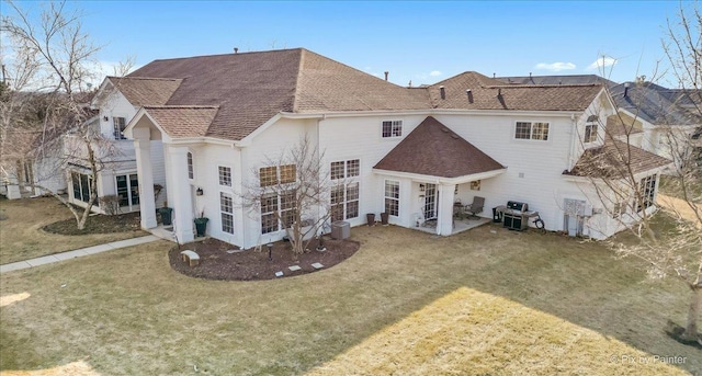 rear view of property featuring a shingled roof, a lawn, and a patio