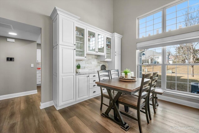 dining space with dark wood-type flooring, visible vents, a towering ceiling, and baseboards