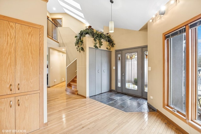 foyer featuring high vaulted ceiling, a skylight, stairway, and wood finished floors