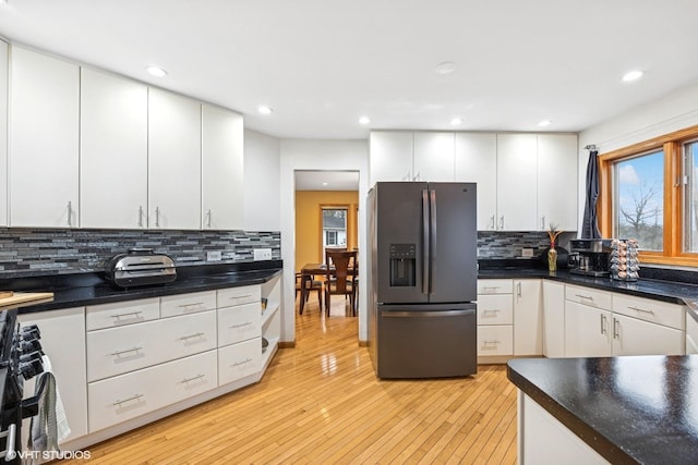 kitchen with stainless steel fridge, tasteful backsplash, white cabinets, dark countertops, and light wood-style flooring