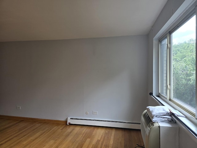 empty room featuring a baseboard heating unit, light wood-style floors, and baseboards