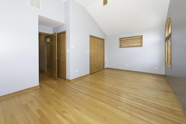 empty room with high vaulted ceiling, visible vents, light wood-style flooring, and baseboards