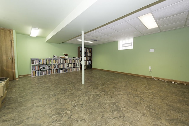 basement with a paneled ceiling and baseboards