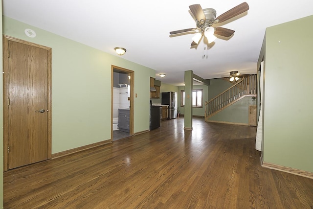 unfurnished living room featuring dark wood-style flooring, ceiling fan, baseboards, and stairs