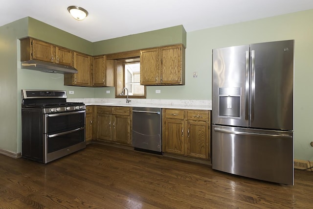 kitchen with appliances with stainless steel finishes, light countertops, under cabinet range hood, and dark wood-type flooring