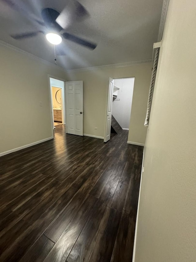 empty room featuring a ceiling fan, baseboards, dark wood-style flooring, and ornamental molding