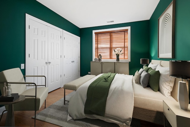 bedroom featuring multiple closets, visible vents, and wood finished floors