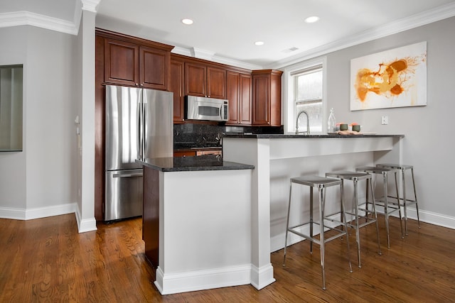 kitchen featuring a breakfast bar area, a peninsula, appliances with stainless steel finishes, dark wood-style floors, and tasteful backsplash