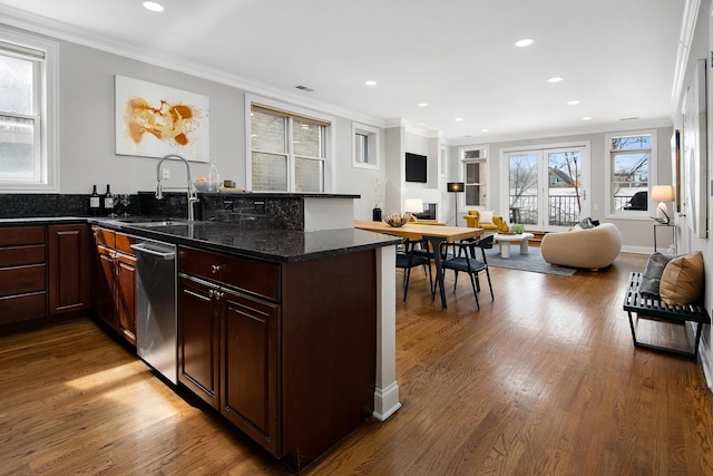 kitchen featuring wood finished floors, a sink, open floor plan, ornamental molding, and dark stone counters