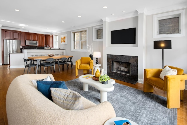 living area with a fireplace, recessed lighting, ornamental molding, wood finished floors, and baseboards