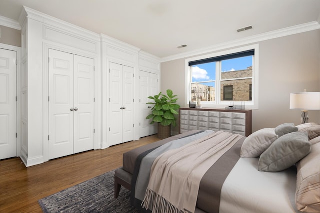 bedroom with crown molding, wood finished floors, visible vents, and multiple closets