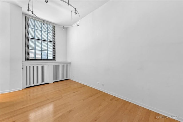 empty room featuring baseboards, rail lighting, radiator heating unit, and wood finished floors