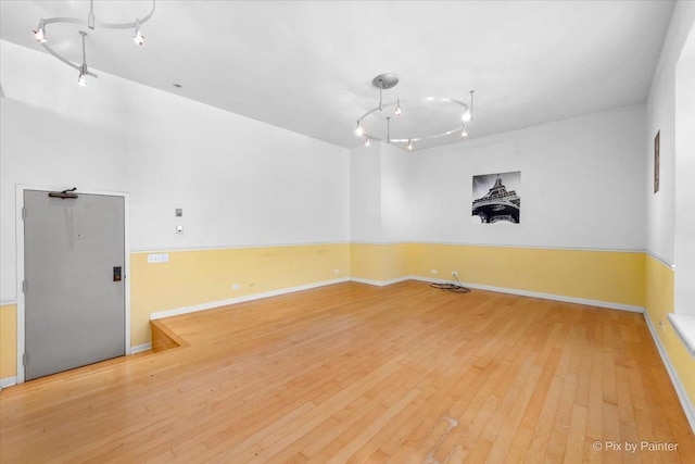 empty room featuring wood-type flooring, baseboards, and track lighting