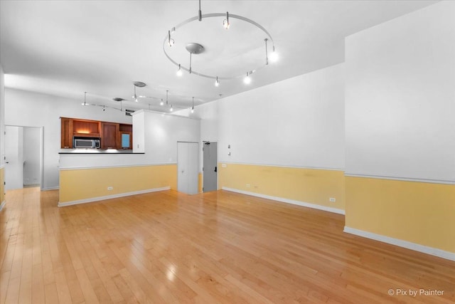 unfurnished living room with light wood-type flooring, rail lighting, and baseboards