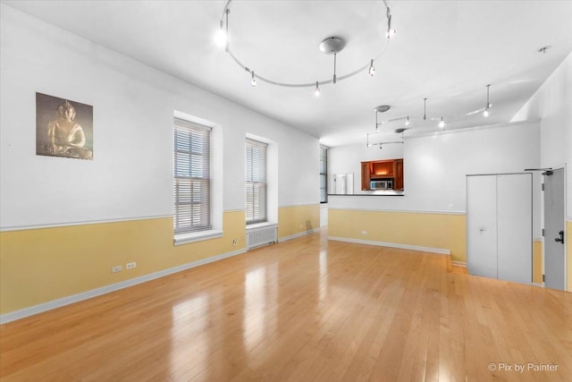 empty room featuring light wood-type flooring, rail lighting, radiator heating unit, and baseboards