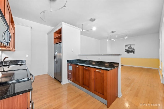 kitchen with light wood-style floors, dark stone counters, stainless steel fridge, and a sink