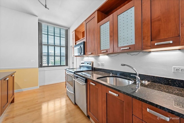 kitchen with brown cabinets, dark stone countertops, stainless steel appliances, light wood-type flooring, and a sink