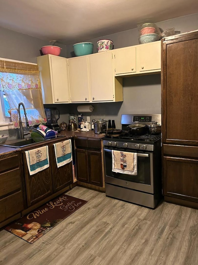 kitchen with a sink, white cabinetry, stainless steel range with gas cooktop, and light wood finished floors