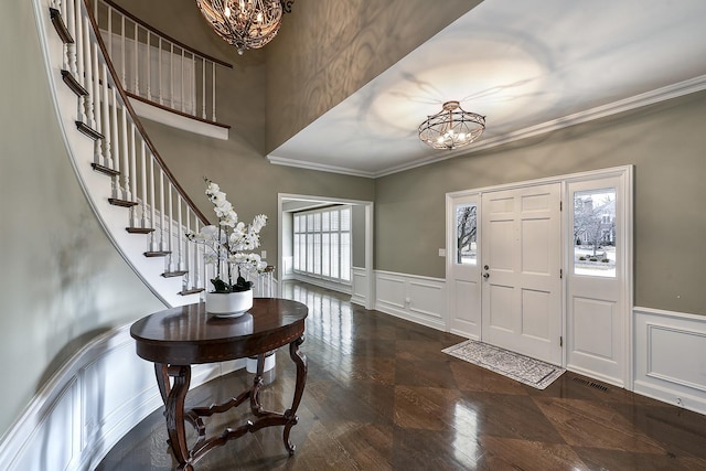 foyer entrance with a chandelier, crown molding, a decorative wall, and stairs