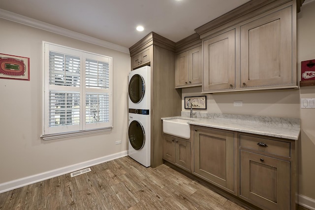 clothes washing area with cabinet space, visible vents, light wood-style flooring, stacked washer / drying machine, and a sink