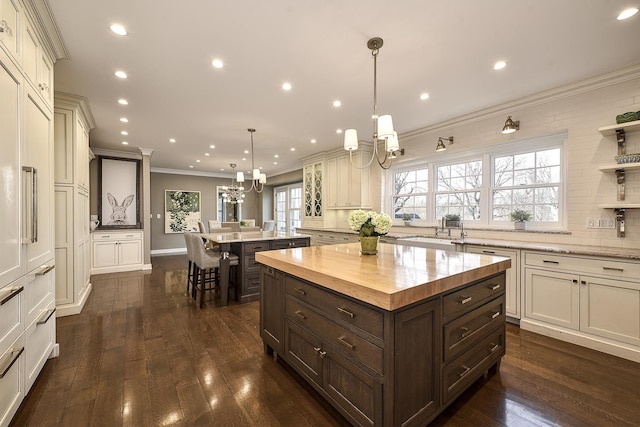 kitchen with a notable chandelier, backsplash, ornamental molding, a kitchen island, and dark brown cabinetry