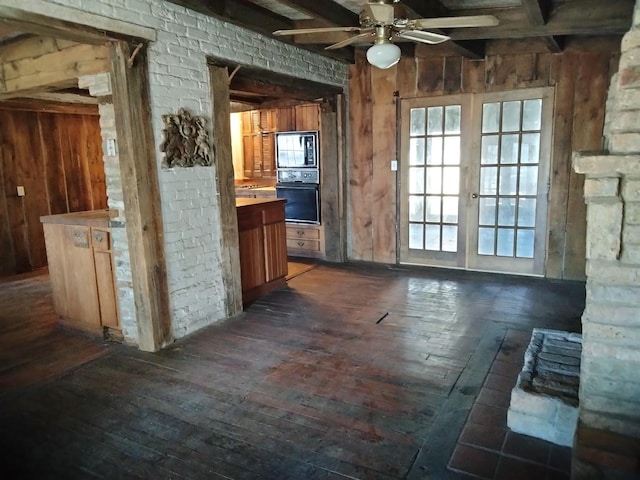 kitchen featuring wooden walls, black oven, dark wood-type flooring, built in microwave, and a ceiling fan