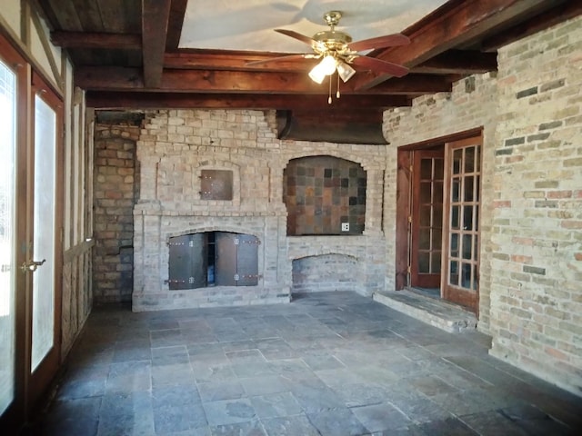 unfurnished living room featuring a ceiling fan, beam ceiling, stone finish floor, an outdoor fireplace, and french doors