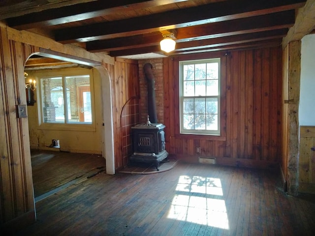 unfurnished living room with beam ceiling, a wood stove, hardwood / wood-style flooring, and arched walkways