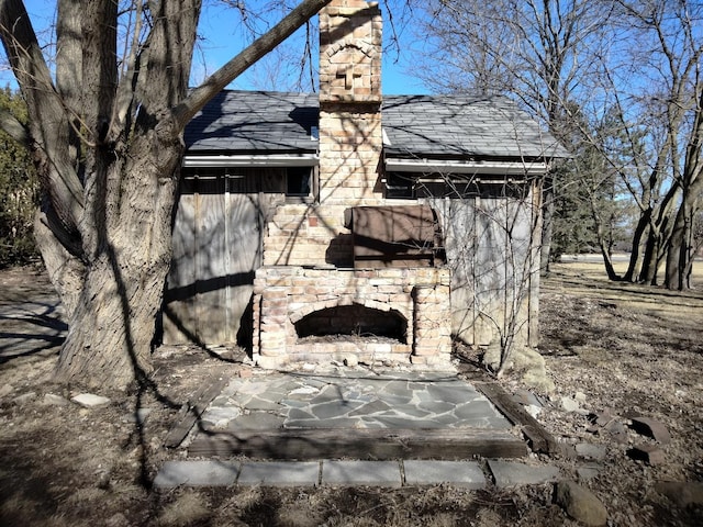 exterior space with exterior fireplace, stone siding, and roof with shingles