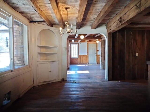 unfurnished dining area featuring beamed ceiling, wood walls, wooden ceiling, an inviting chandelier, and arched walkways