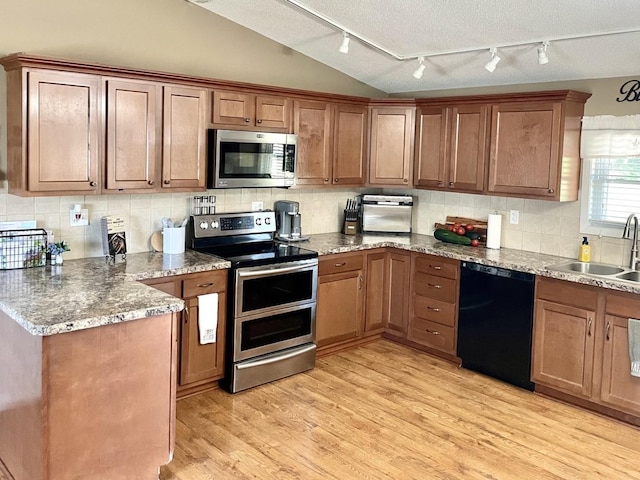 kitchen featuring stainless steel appliances, a sink, vaulted ceiling, light wood finished floors, and tasteful backsplash