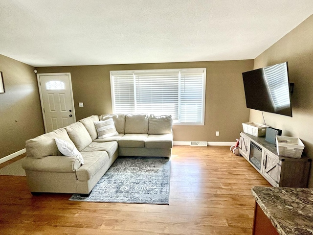 living area with visible vents, a textured ceiling, light wood-style flooring, and baseboards