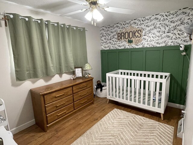 bedroom with ceiling fan, a decorative wall, a wainscoted wall, wood finished floors, and wallpapered walls