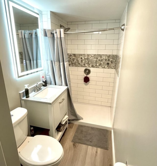 bathroom featuring toilet, a tile shower, wood finished floors, and vanity