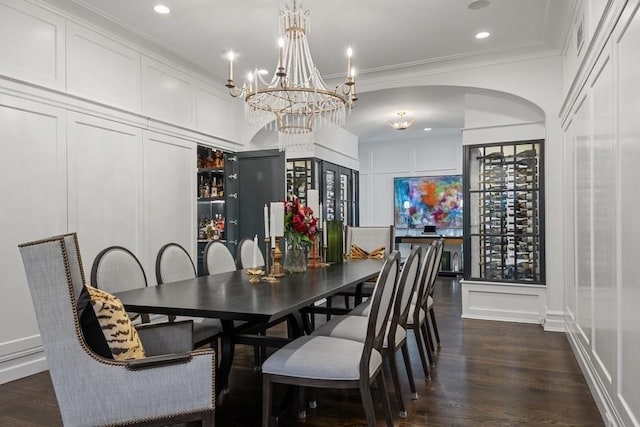 dining area with a decorative wall, dark wood-style floors, arched walkways, and ornamental molding