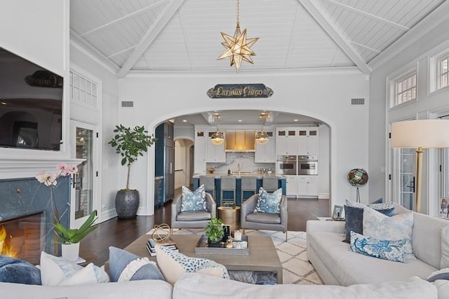 living room featuring a high end fireplace, visible vents, beamed ceiling, and wood finished floors